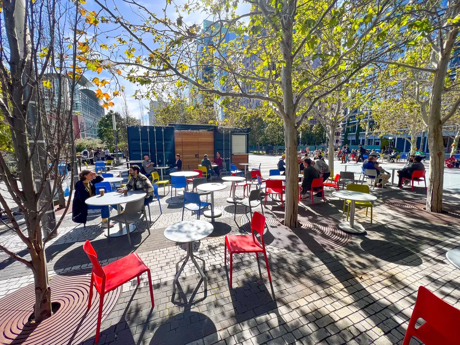 Outdoor patio with colorful chairs and tables shaded by trees at the Salesforce Park beer garden.
