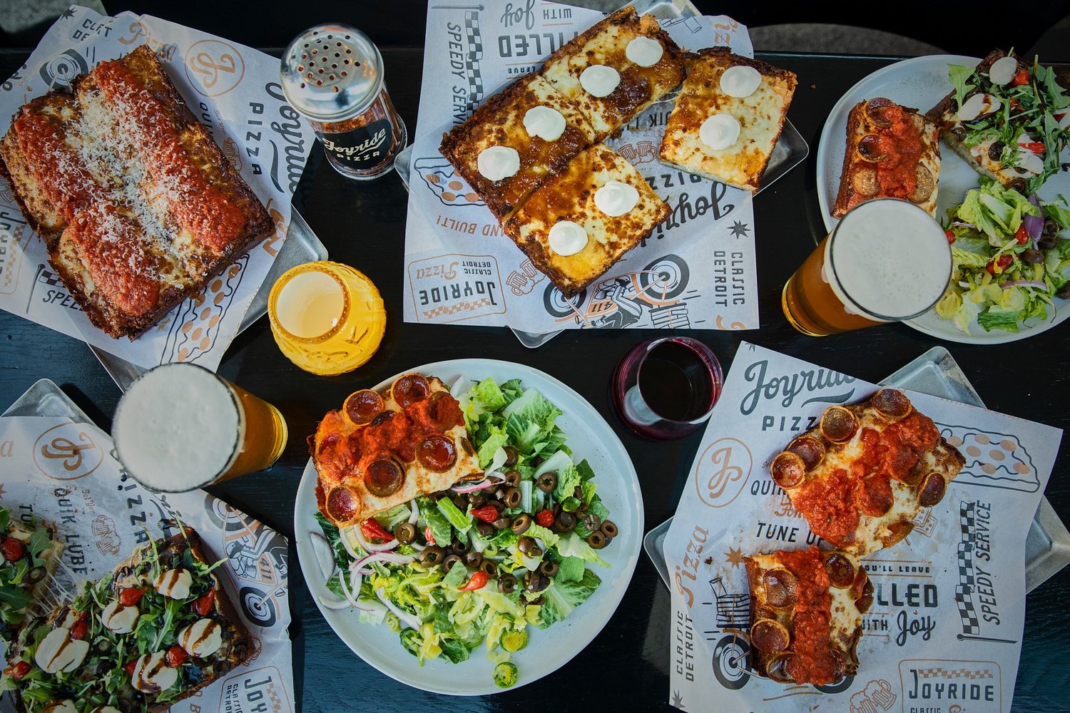 Overhead view of Joyride pizzas, salads and beers spread across a table.